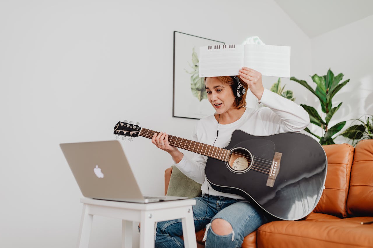 A woman playing guitar during an online class with headphones in her cozy living room.